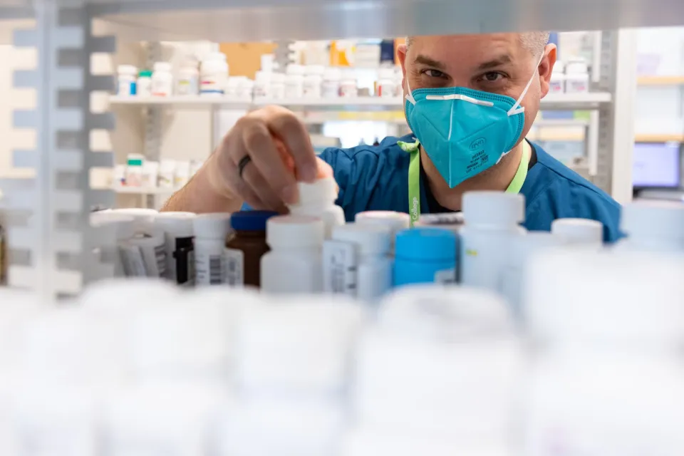 A pharmacy technology student taking a medication bottle from a shelf