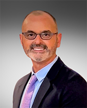 Dr. Scott Latiolais, Vice President of Student Success. Bearded smiling man wearing spectacles, and orchid-colored tie, blue shirt and suit coat.