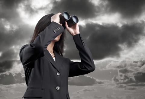A business professional scanning the horizon with binoculars under a dramatic, cloudy sky.”
